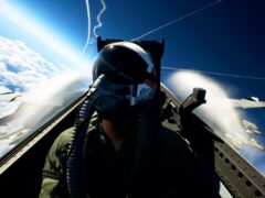 Ace Combat 8 fighter jet banking through clouds above a carrier fleet