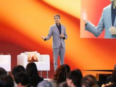 Sony Pictures Entertainment CEO Ravi Ahuja speaking on stage in front of an orange backdrop and a large video screen
